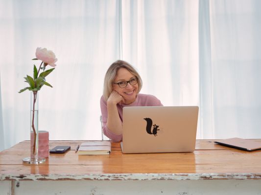 Sabine Läpple sitzt mit Laptop am Schreibtisch und blickt lächelnd in die Kamera – professionelles Branding-Foto für ihre Website.