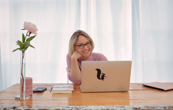 Sabine Läpple sitzt mit Laptop am Schreibtisch und blickt lächelnd in die Kamera – professionelles Branding-Foto für ihre Website.